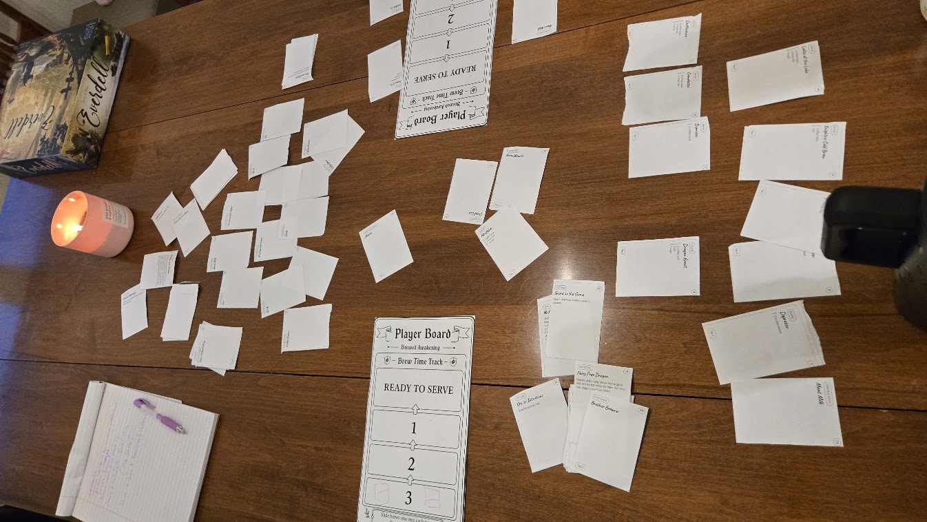 Dozens of hand-cut paper prototype cards laid out across a wooden table.